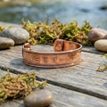 Copper bracelet with engraved patterns on a wooden surface with natural background